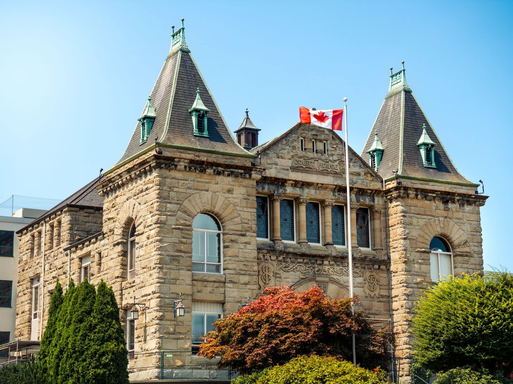 A stone courthouse building with a Canadian flag flying outside.