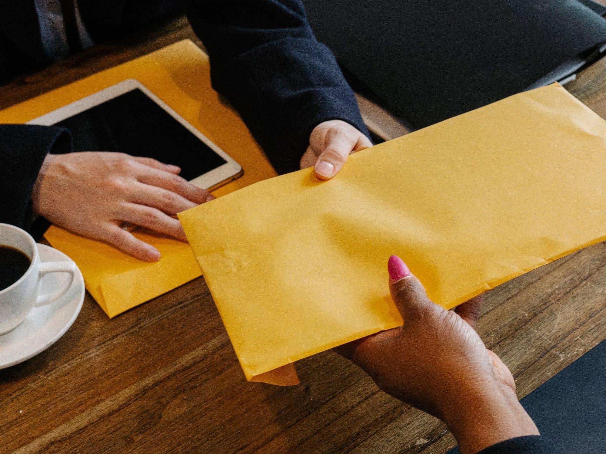 Two people passing a large document envelope across a desk.