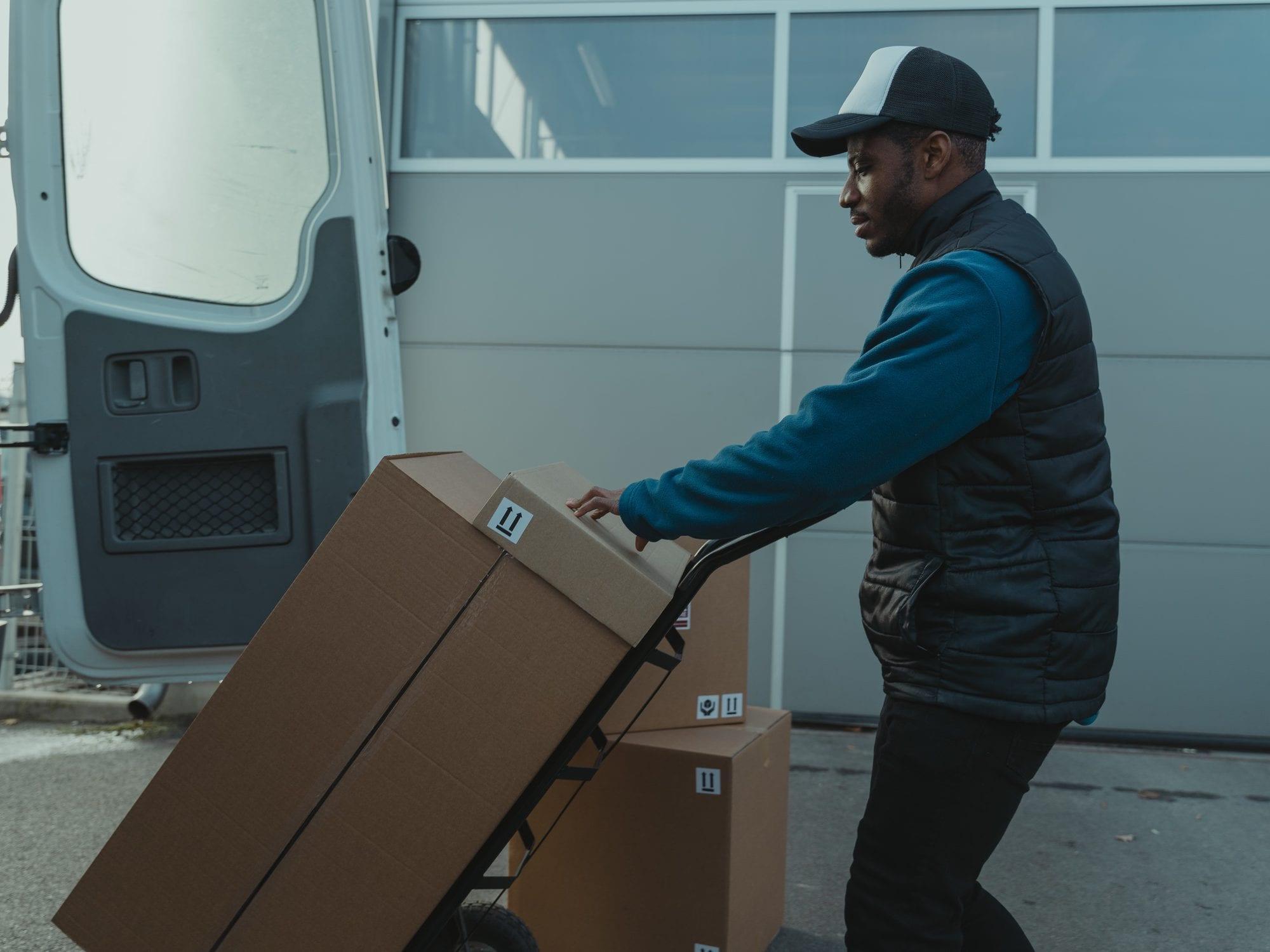 A person moving boxes on a hand truck from a delivery van.